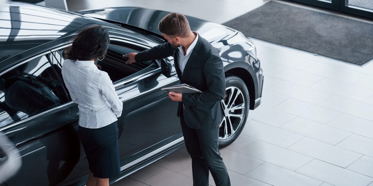 Looking at vehicle interior. Female customer and modern stylish bearded businessman in the automobile saloon.