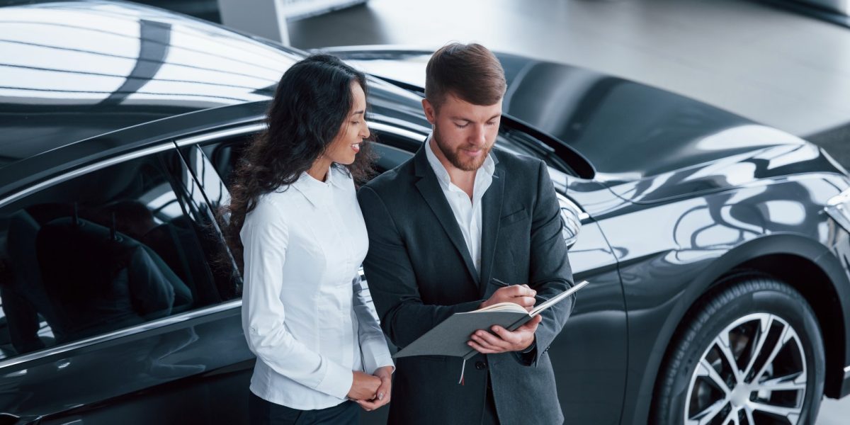 Filling the documents. Female customer and modern stylish bearded businessman in the automobile saloon.